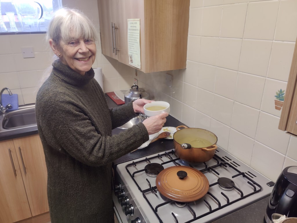 Cook serving soup from a pan on the hob for Soup Lunch